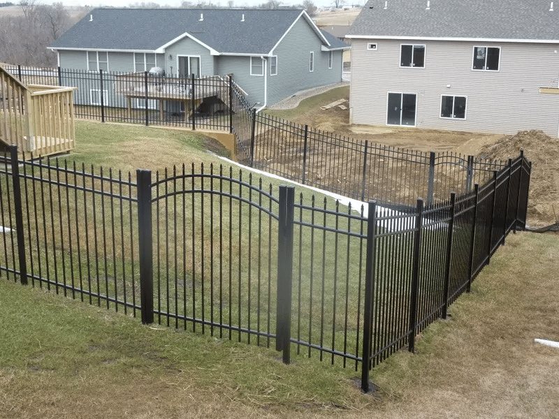 An aluminum fence in a wrought iron style surrounds a backyard.