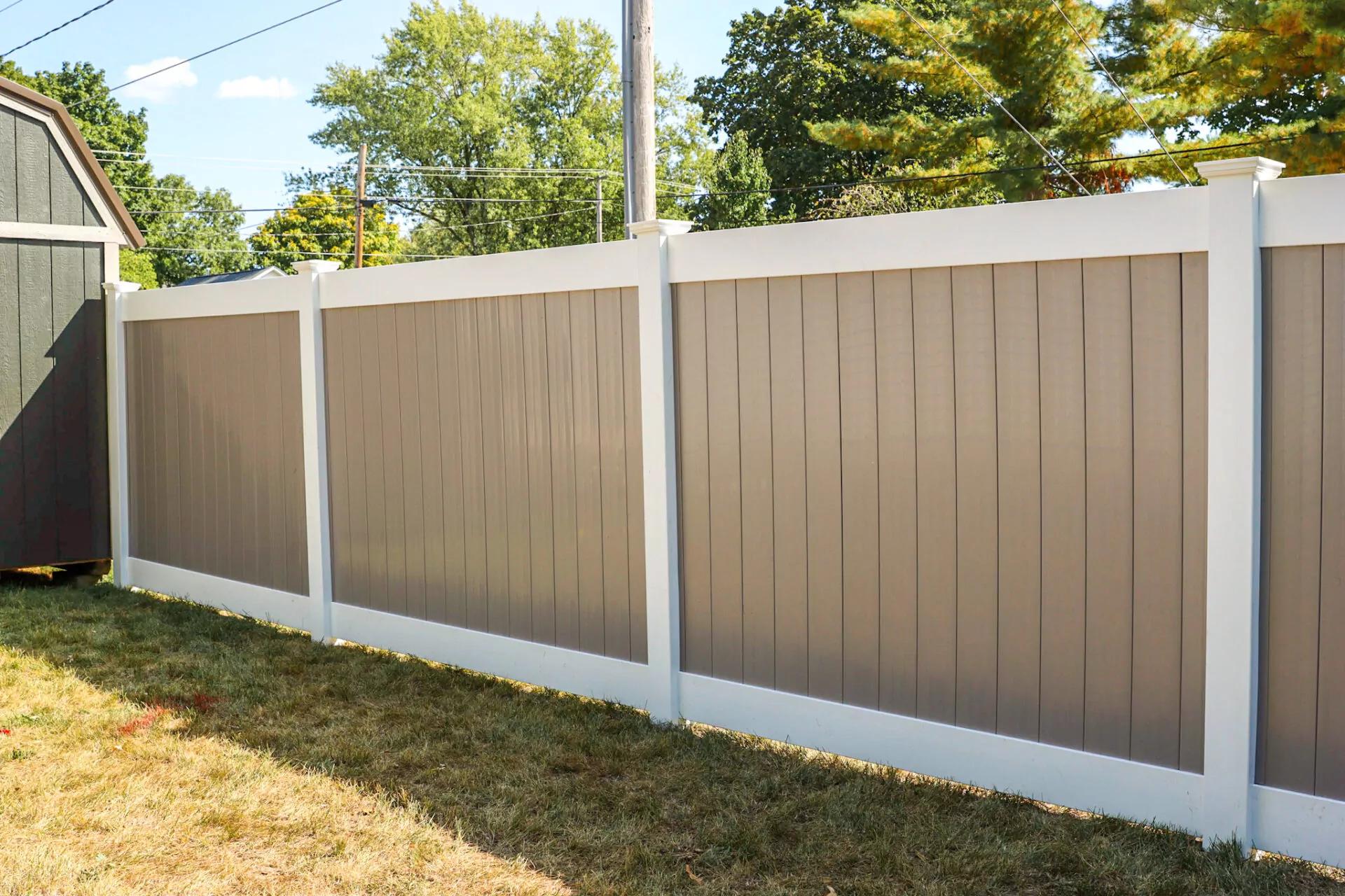 A tall vinyl privacy fence in mocha brown, with white framing and posts.