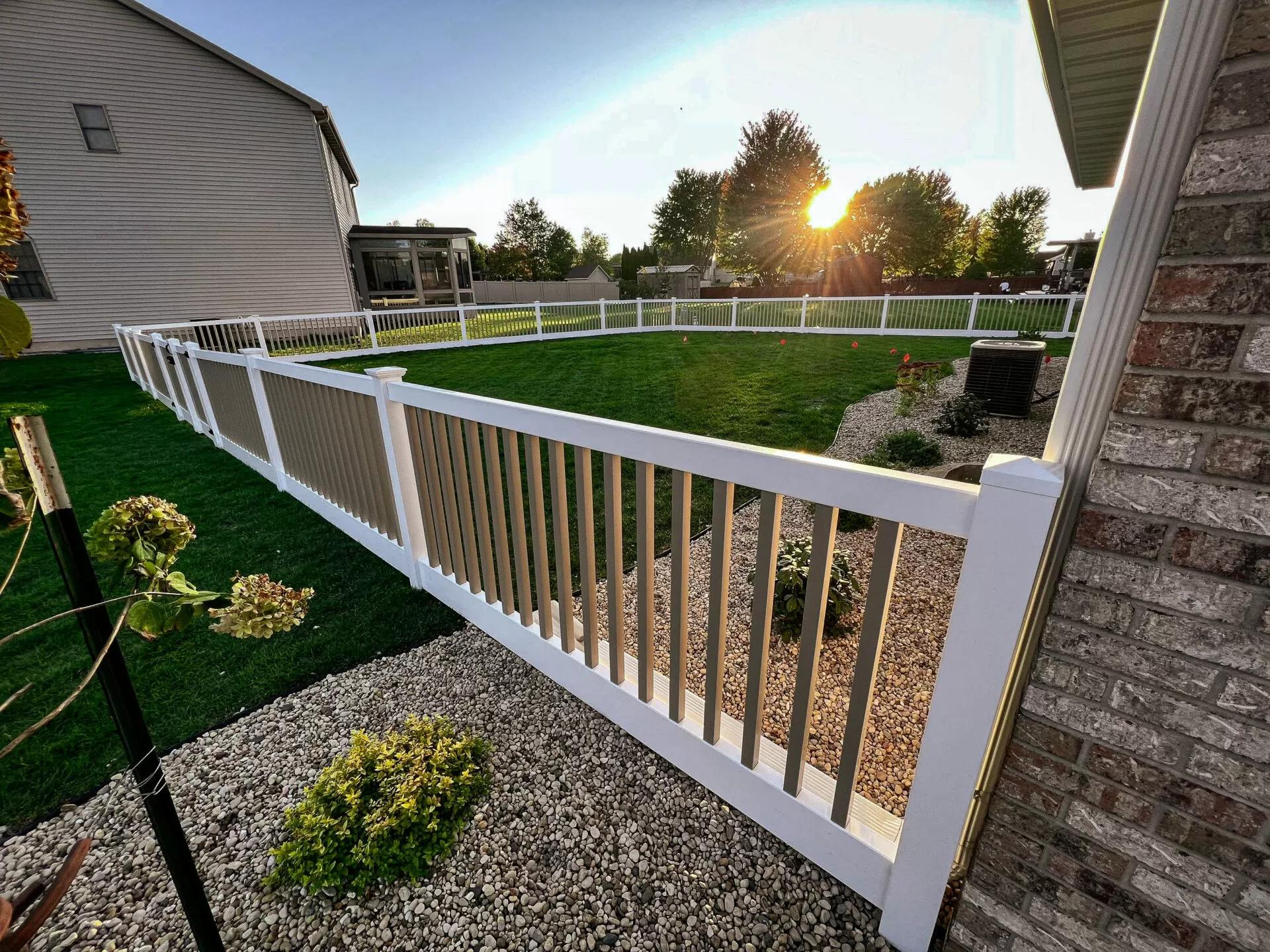 White vinyl fence along a landscaped yard at sunset