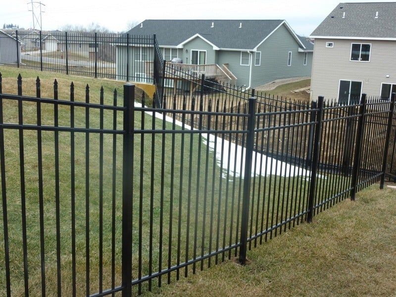 An aluminum fence in a wrought iron style surrounding a backyard.