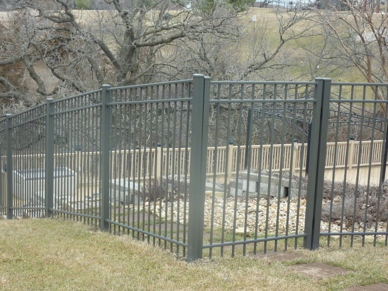A medium grey aluminum fence borders a landscaped rock garden with benches.