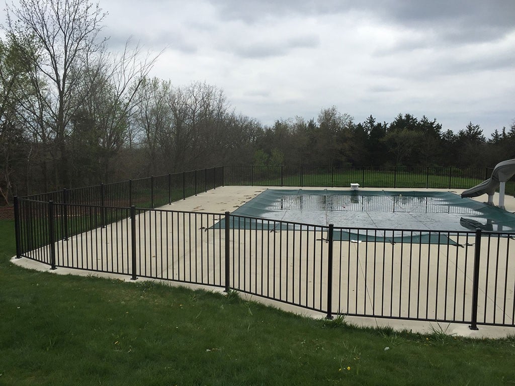 A black aluminum fence surrounds a swimming pool and concrete pool deck.