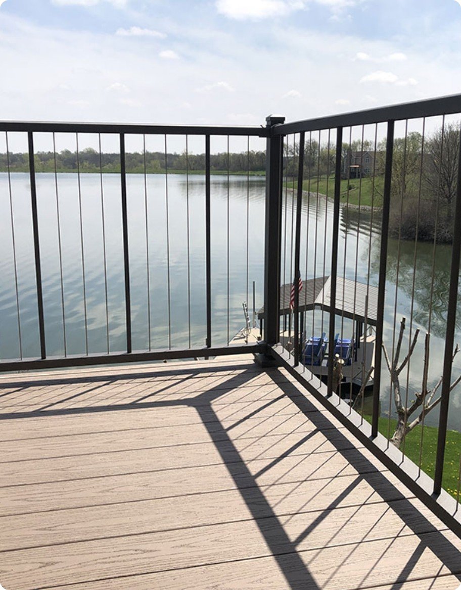 A blonde wood-look deck with black VertiCable railing overlooking a lake.