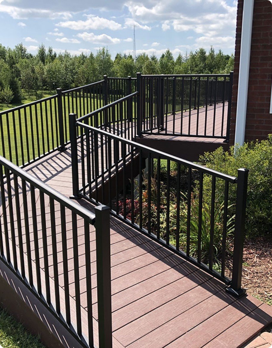 A wheelchair ramp and deck with black aluminum railings in a wrought iron style.