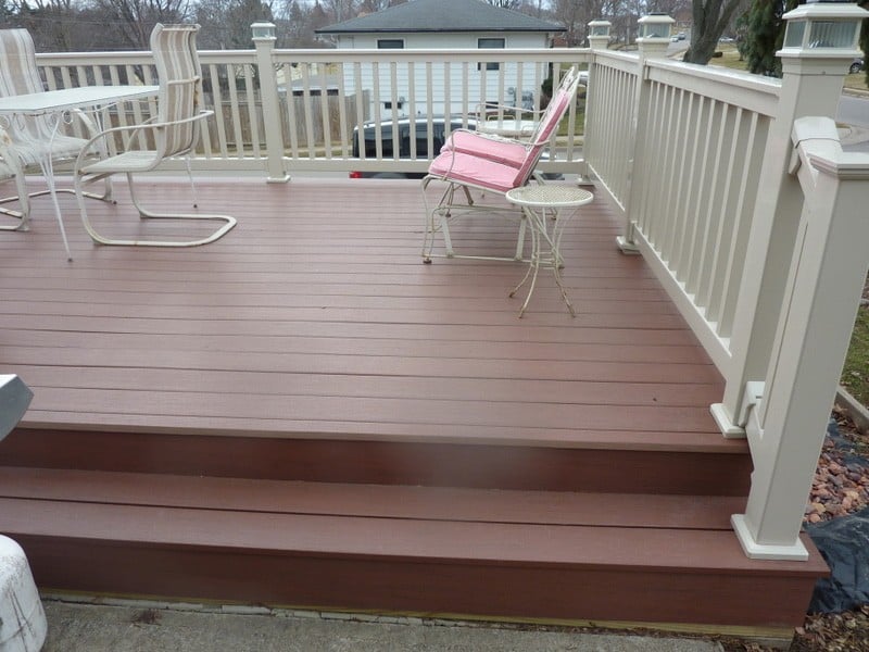 A brown deck surrounded by a white vinyl railing with solar lighting caps.