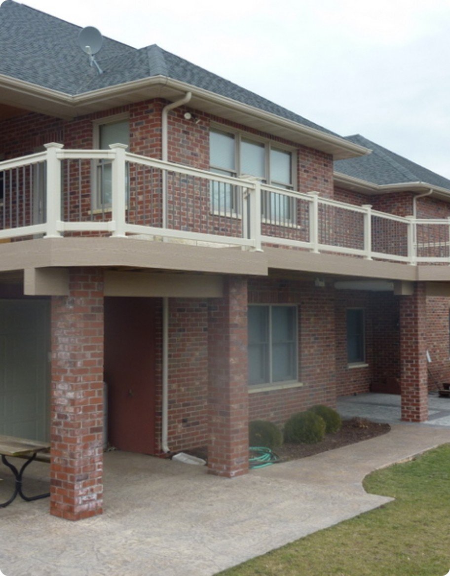 A tan second story balcony with beige vinyl railings on a red brick building.