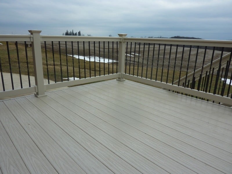 A beige deck with black wrought-iron style railing supports on a winter day.