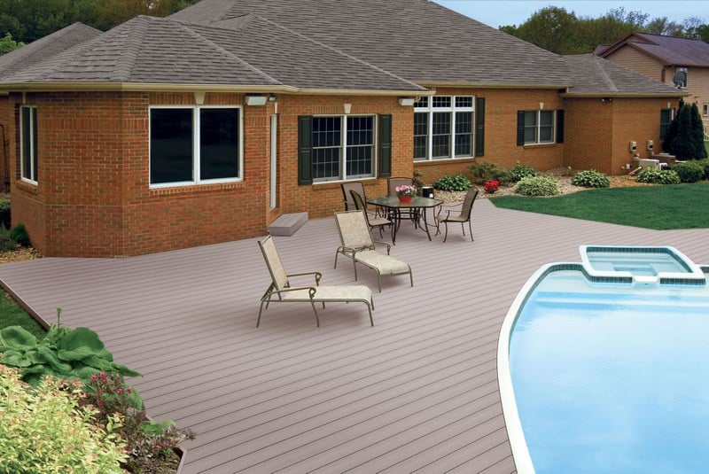 A red-brown deck surrounds a blue swimming pool behind a red brick home.
