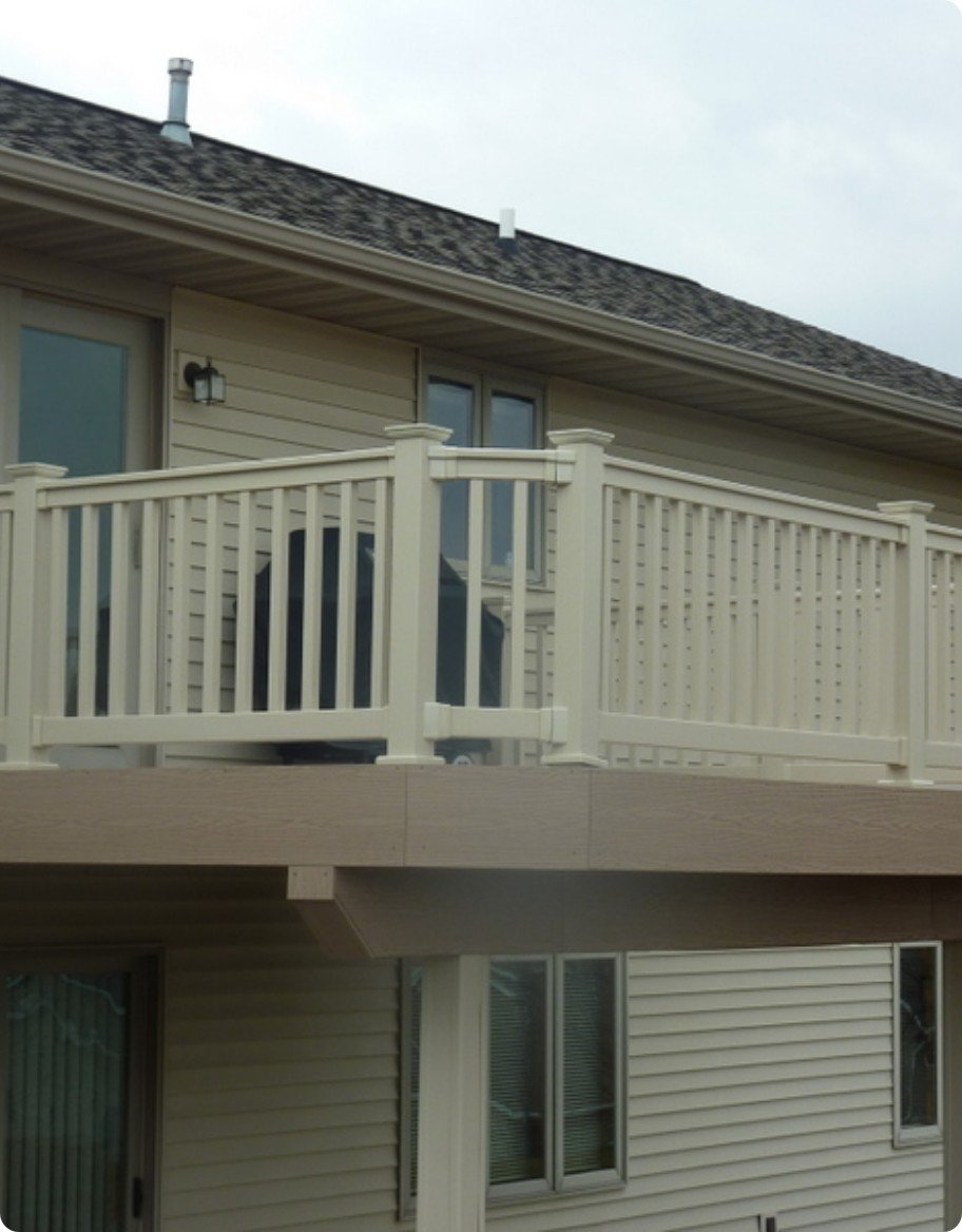 A tan balcony-style deck with beige vinyl railings and a gas grill.