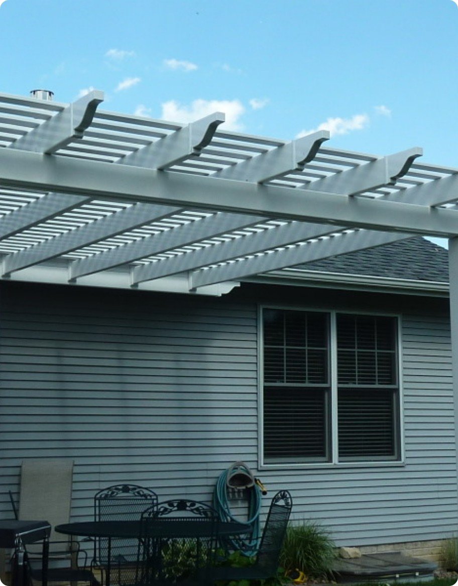 A light gray vinyl pergola over a patio with a wrought iron style dining set.