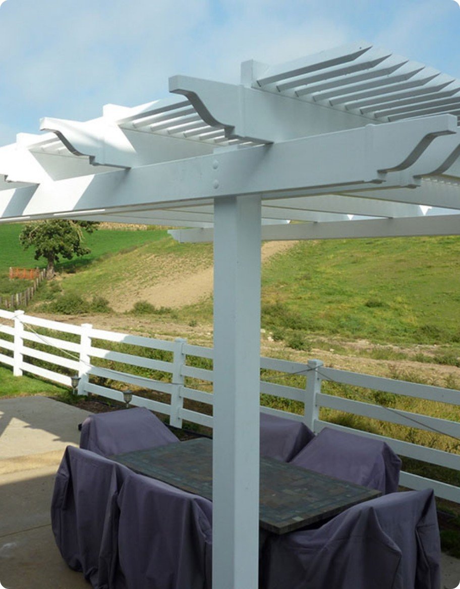 A white vinyl pergola over a concrete patio with an outdoor dining set.