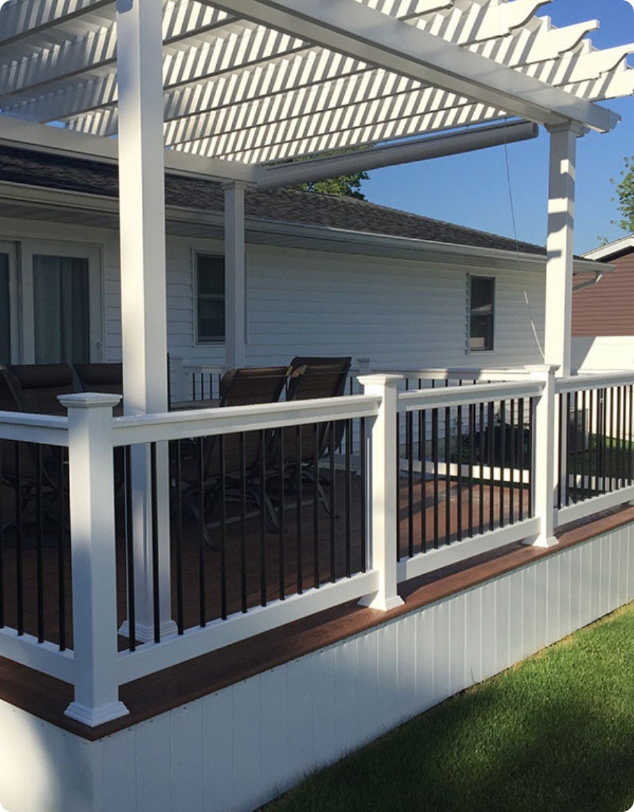 A brown deck with white vinyl railings and a white vinyl pergola.