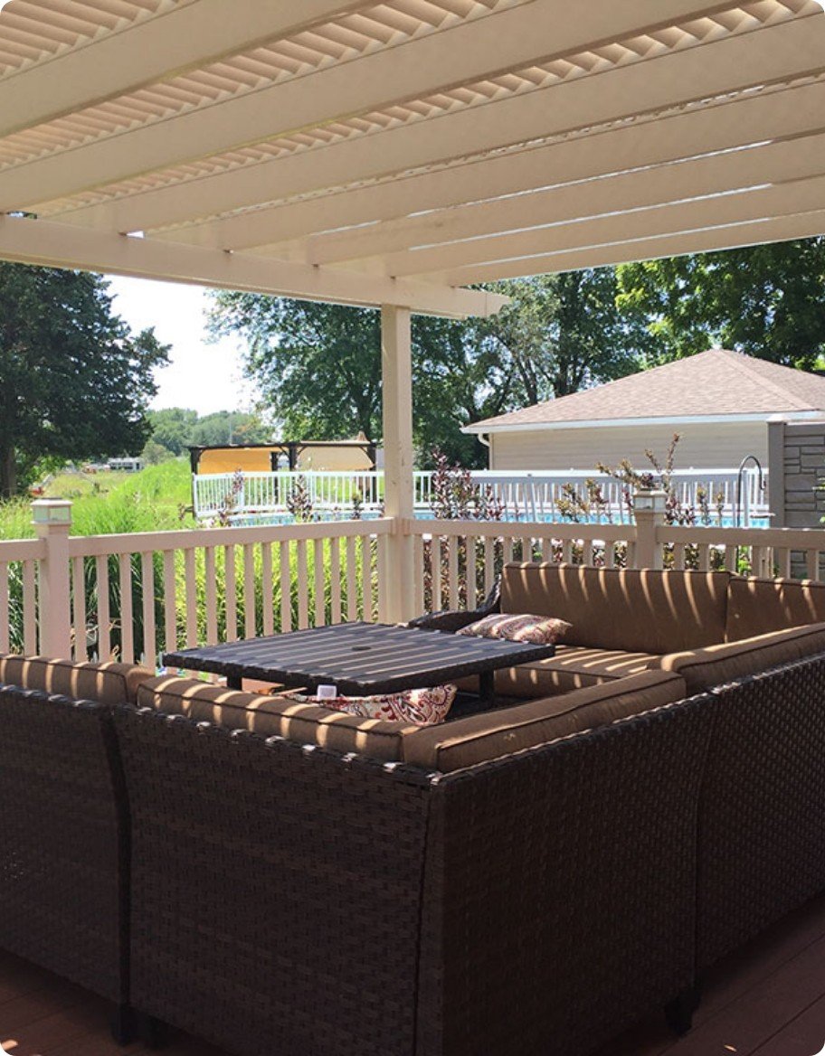 Outdoor sofas on a brown deck under a beige vinyl pergola.