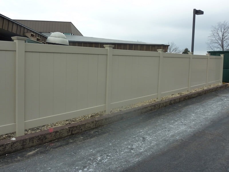 A tall beige vinyl fence along an asphalt street.