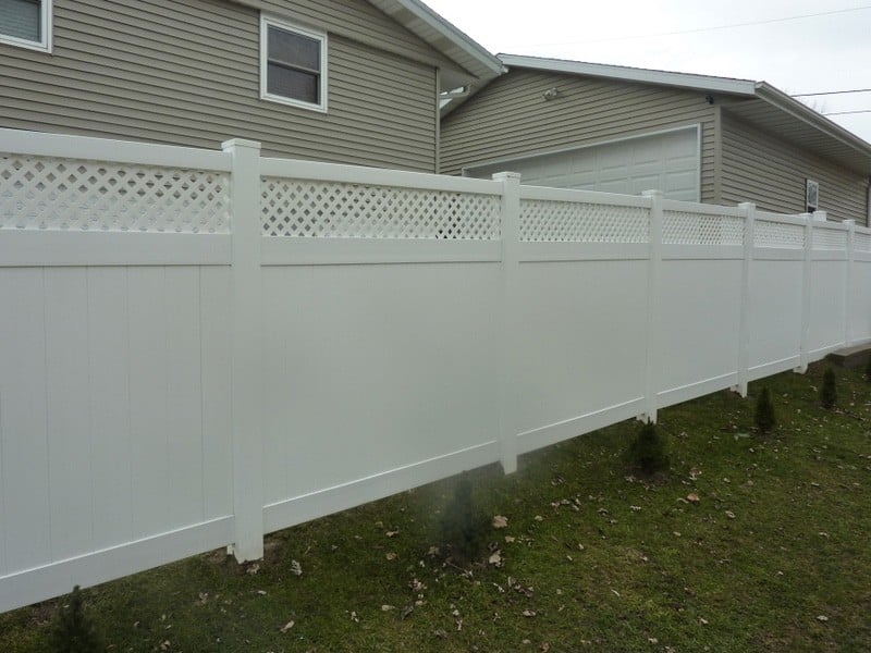 A white vinyl privacy fence with a custom latticework top borders a backyard.