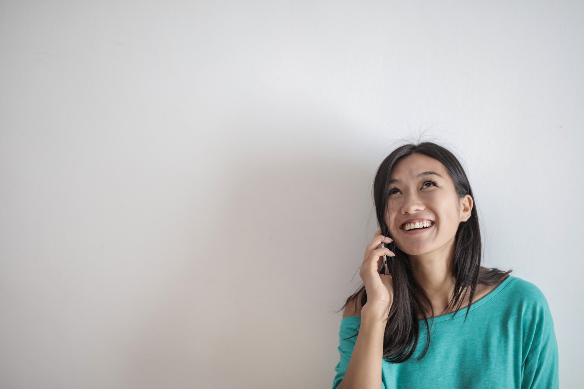 A smiling woman in a teal shirt makes a phone call.