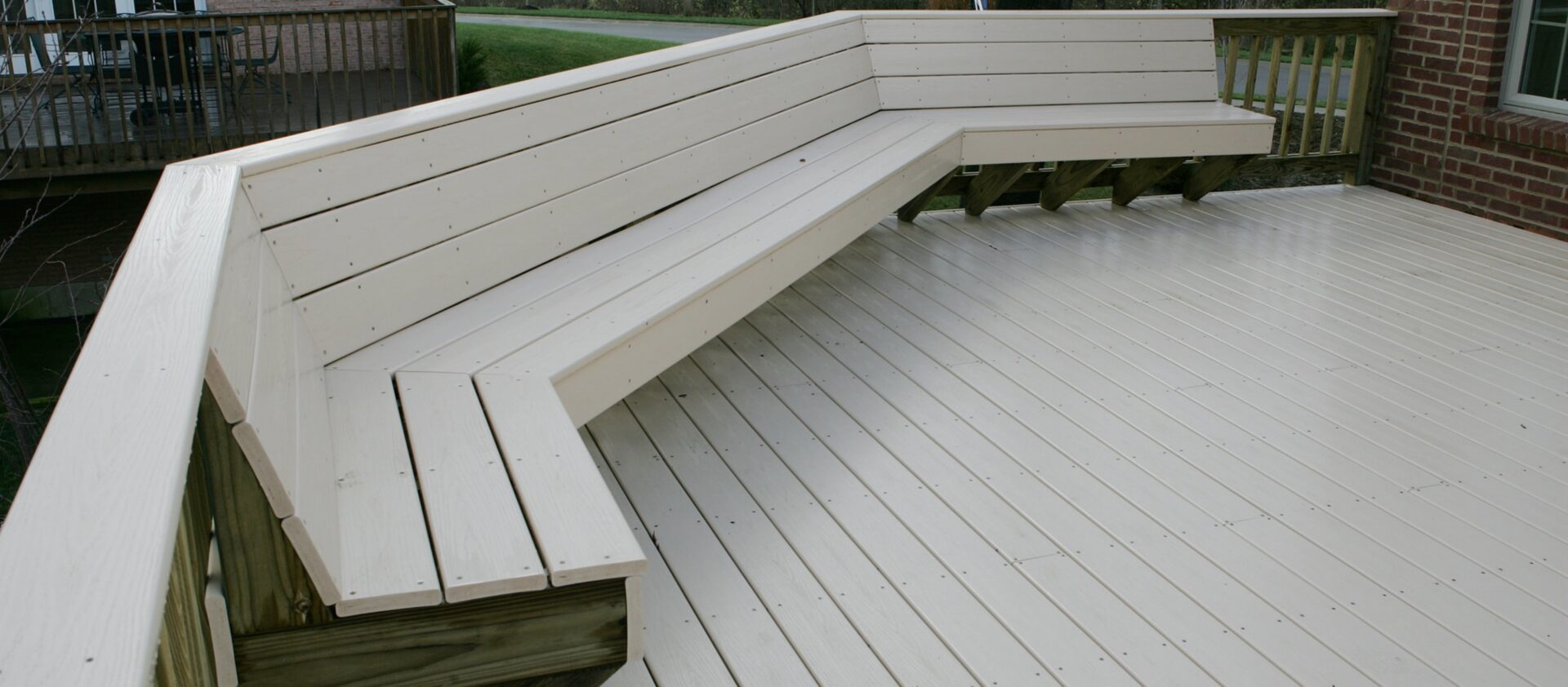 A white premium deck with a built-in bench, attached to a red brick house.