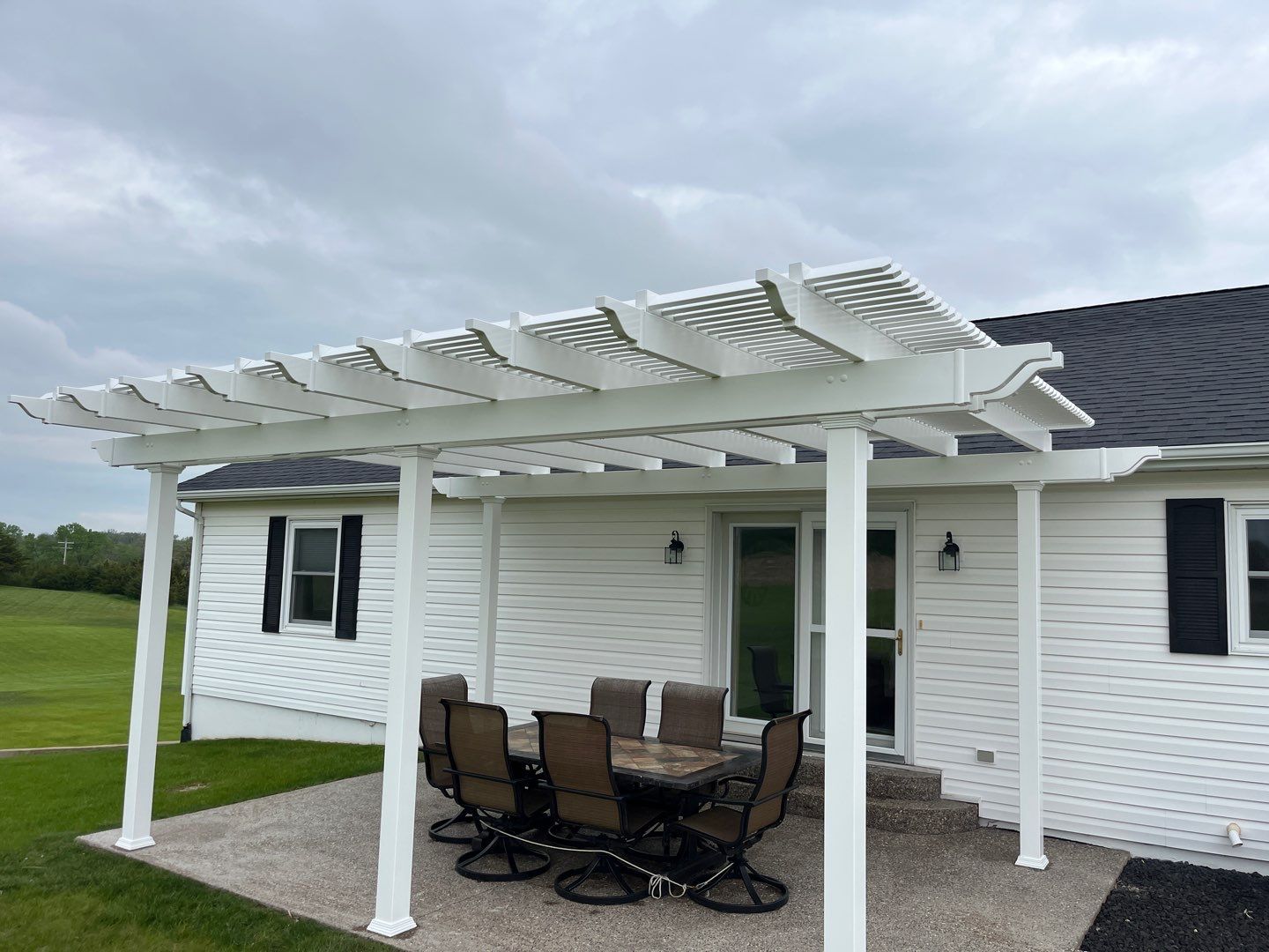 A white house with a patio and white vinyl pergola over an elegant outdoor table set.