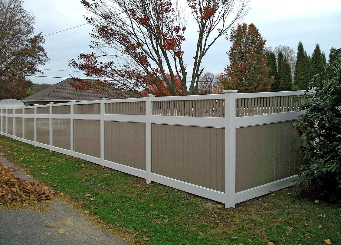 A custom vinyl fence in tan and white with a barred section at the top, in an autumn yard.