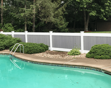 A gray and white vinyl privacy fence behind an in-ground pool with landscaping.
