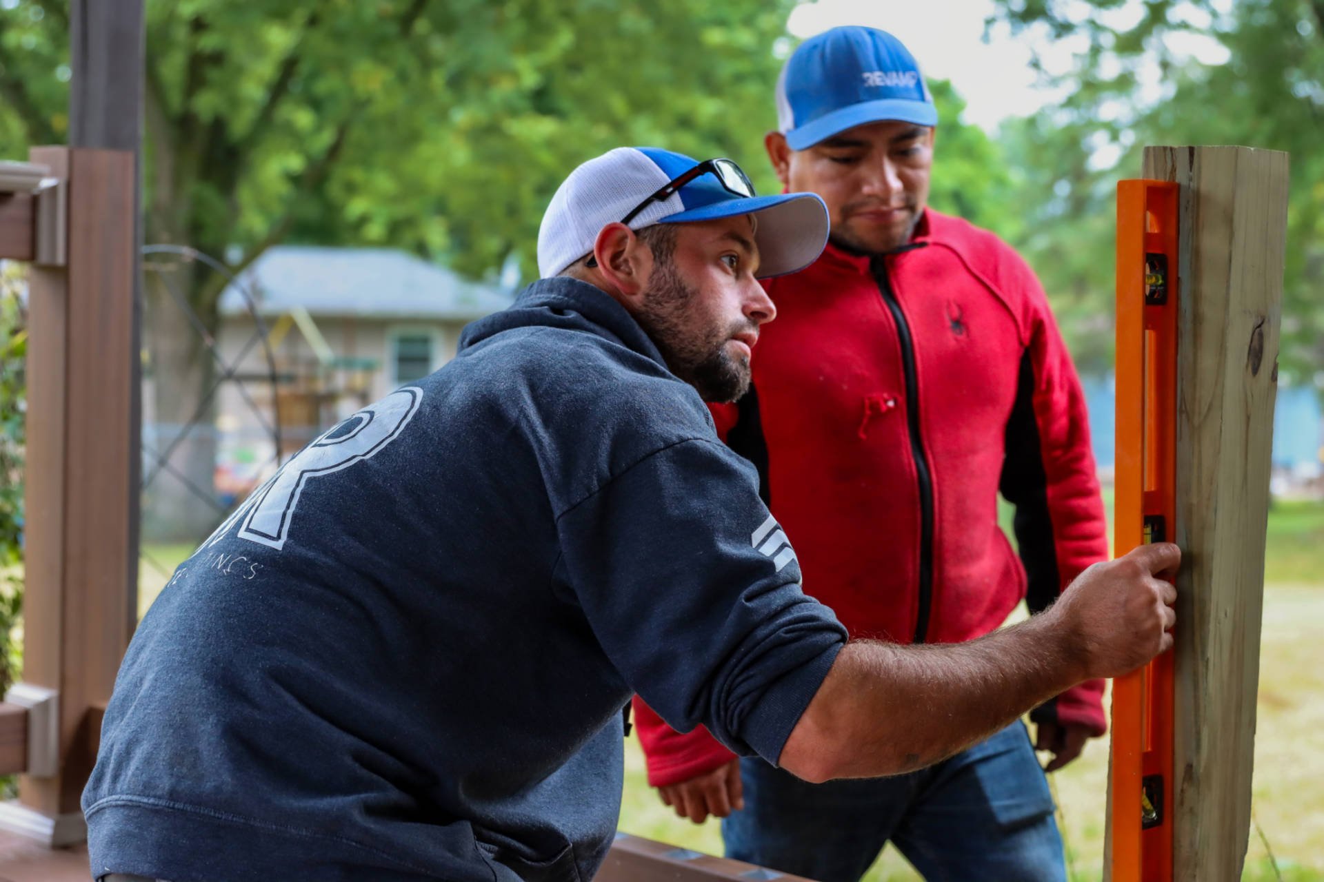 A crew member using a level to check a fence post while another watches.