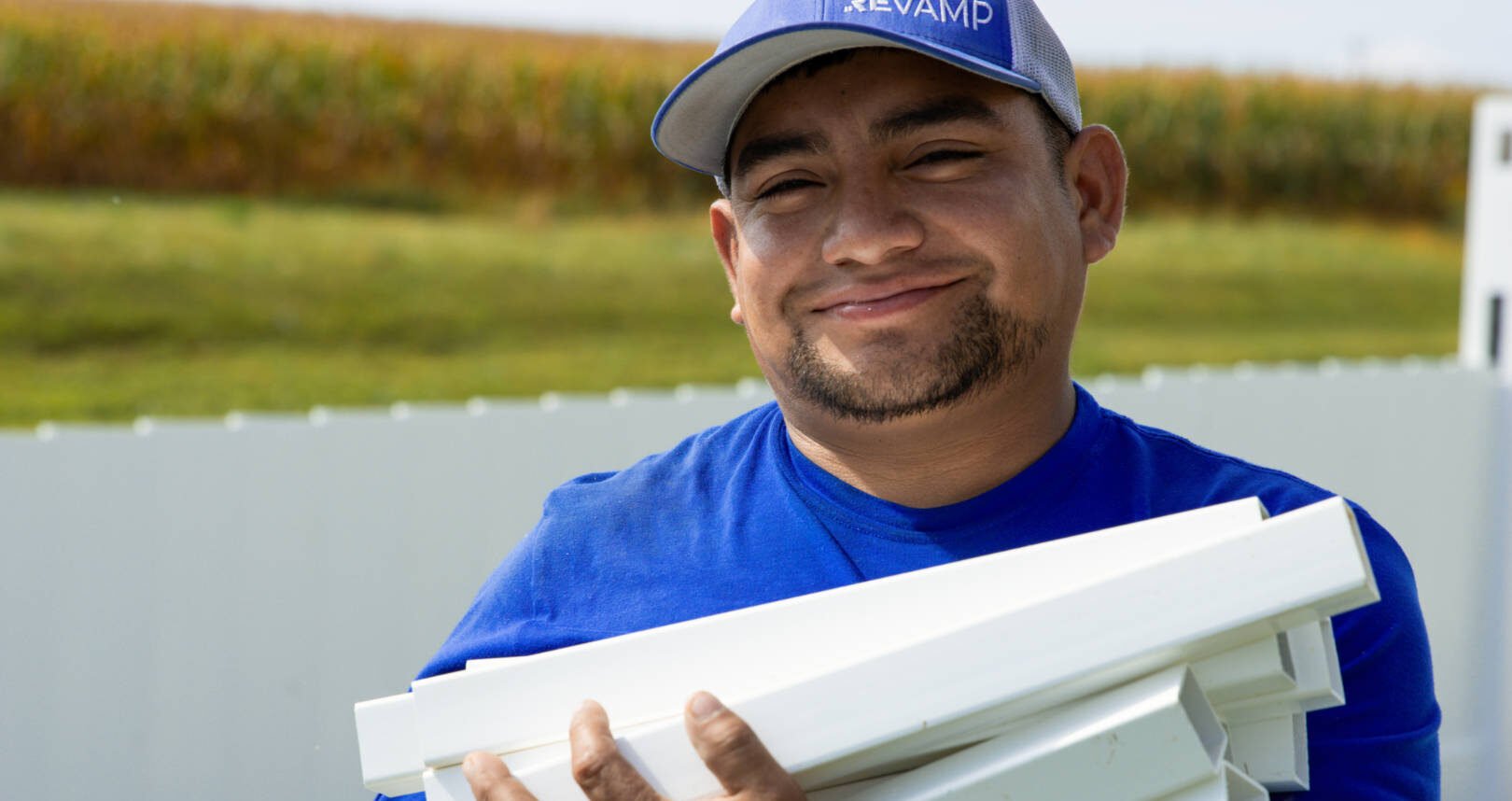 A ReVamp crew member smiling while holding fence panels in front of a white vinyl fence.
