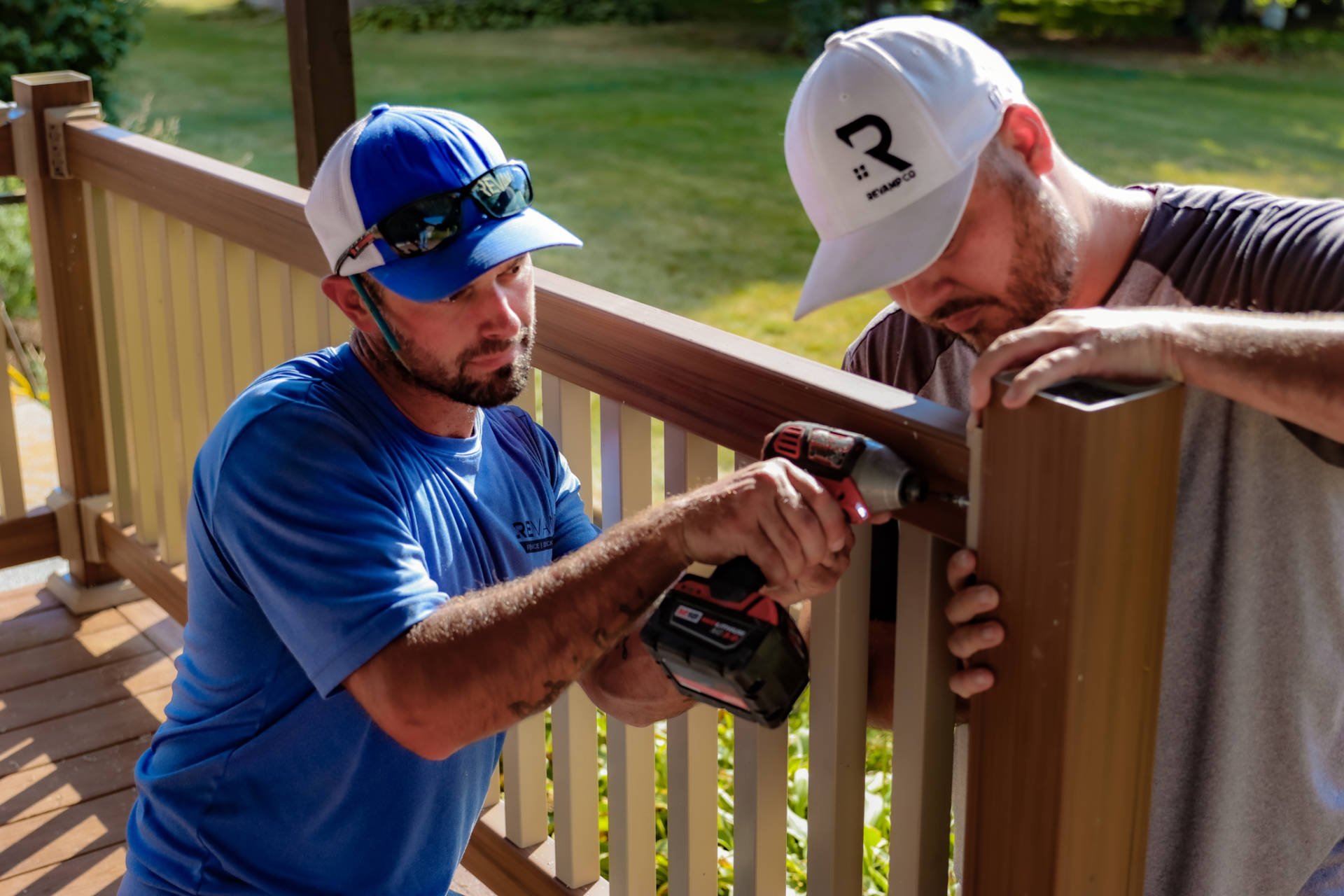 Two crew members drilling in a deck railing post together.